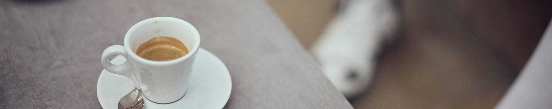 Ein Cappuccino und ein Verlängerter im Hintergrund sieht man Füße mit Radschuhen.