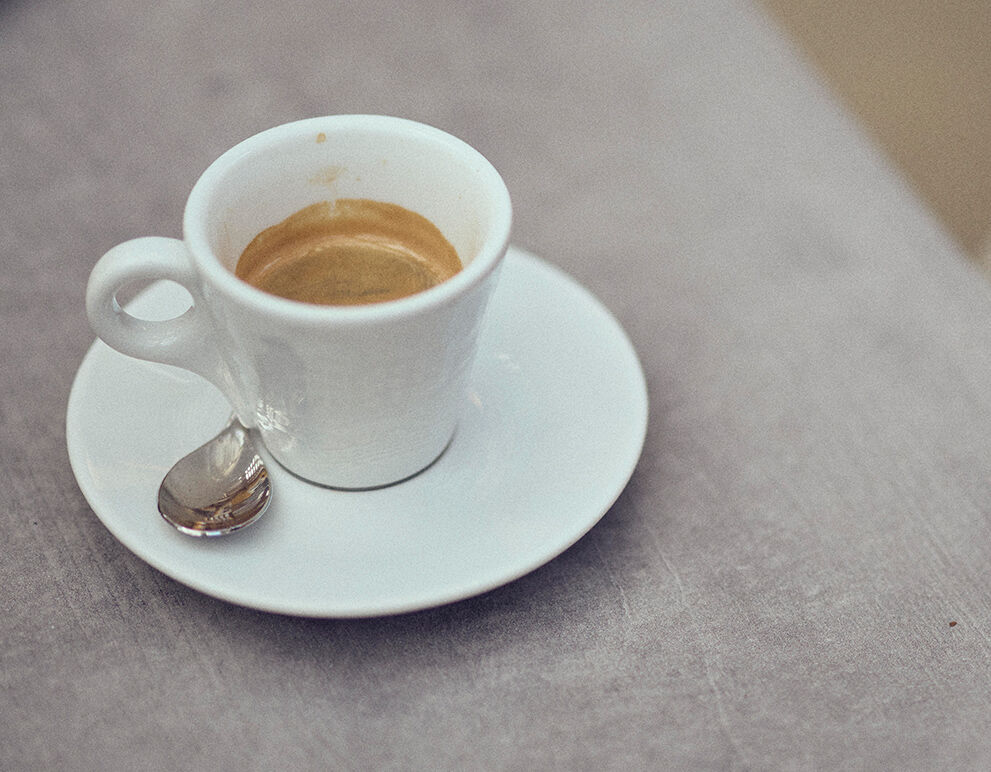 Ein Cappuccino und ein Verlängerter im Hintergrund sieht man Füße mit Radschuhen.